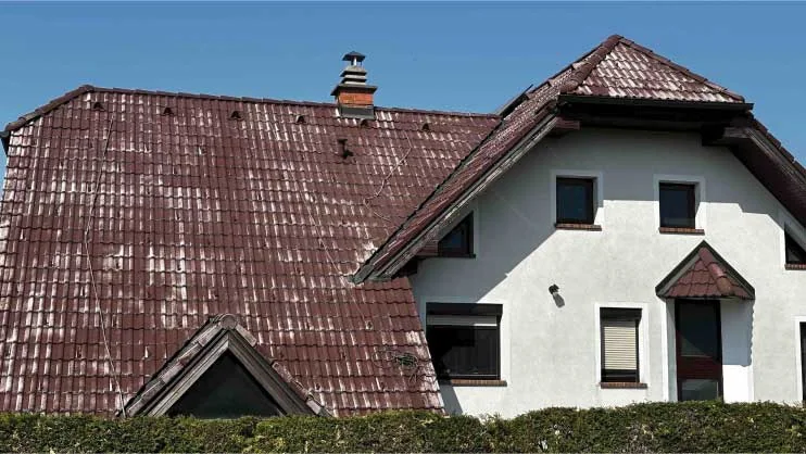 Rdeča streha z vidno obrabo pred obnovo na beli hiši z izrazitim čelnim zatrepom.
